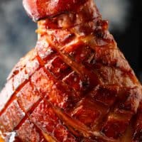 This close-up shot of beautifully glazed ham, its surface glistening with a rich, caramelized coating. The ham has been meticulously scored in a diamond pattern, allowing the glaze to penetrate the meat and create tantalizing crevices of flavor. The deep, reddish-brown hue suggests a savory and slightly sweet profile. A generous amount of glaze pools around the base, inviting you to savor its deliciousness. The background is a dark gray, providing a neutral canvas that accentuates the ham's visual appeal.
