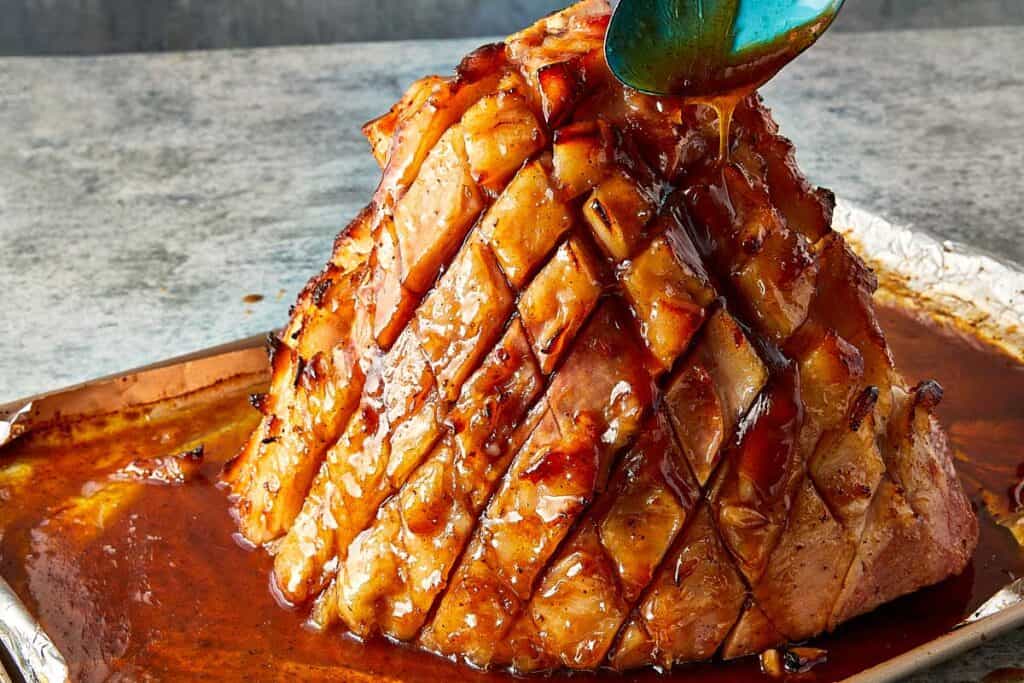 a side view of a cooked ham with glaze being poured on top of it