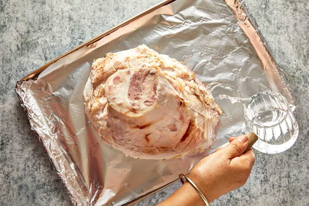 a top down view of a leg ham sitting on aluminum foil, the leg is sitting cut side down looking like a mountain from top down and exposing the fatty layer