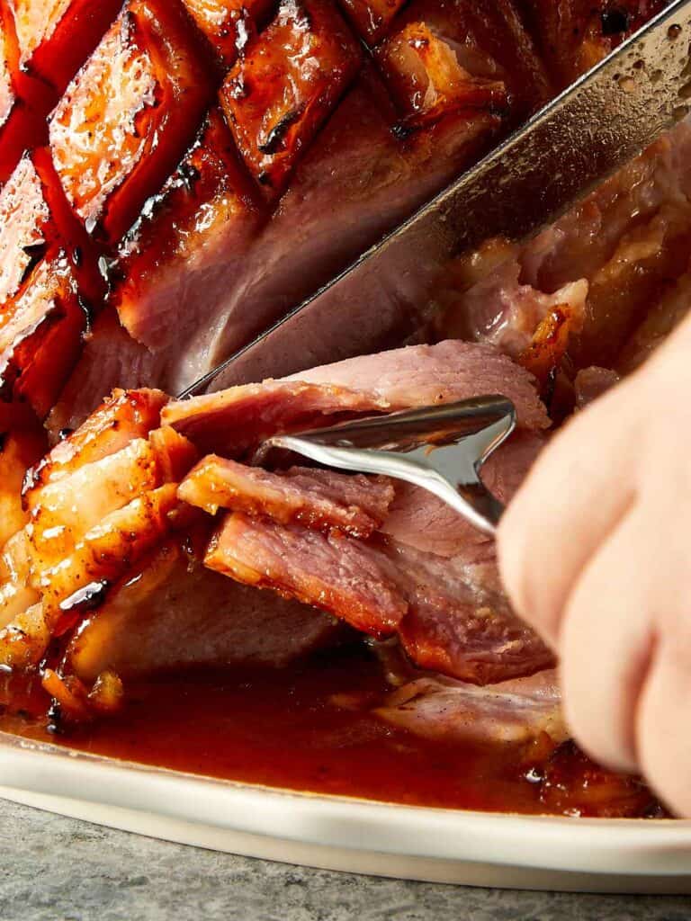 a side view of leg ham with a fork and a knife cutting the leg ham in slices