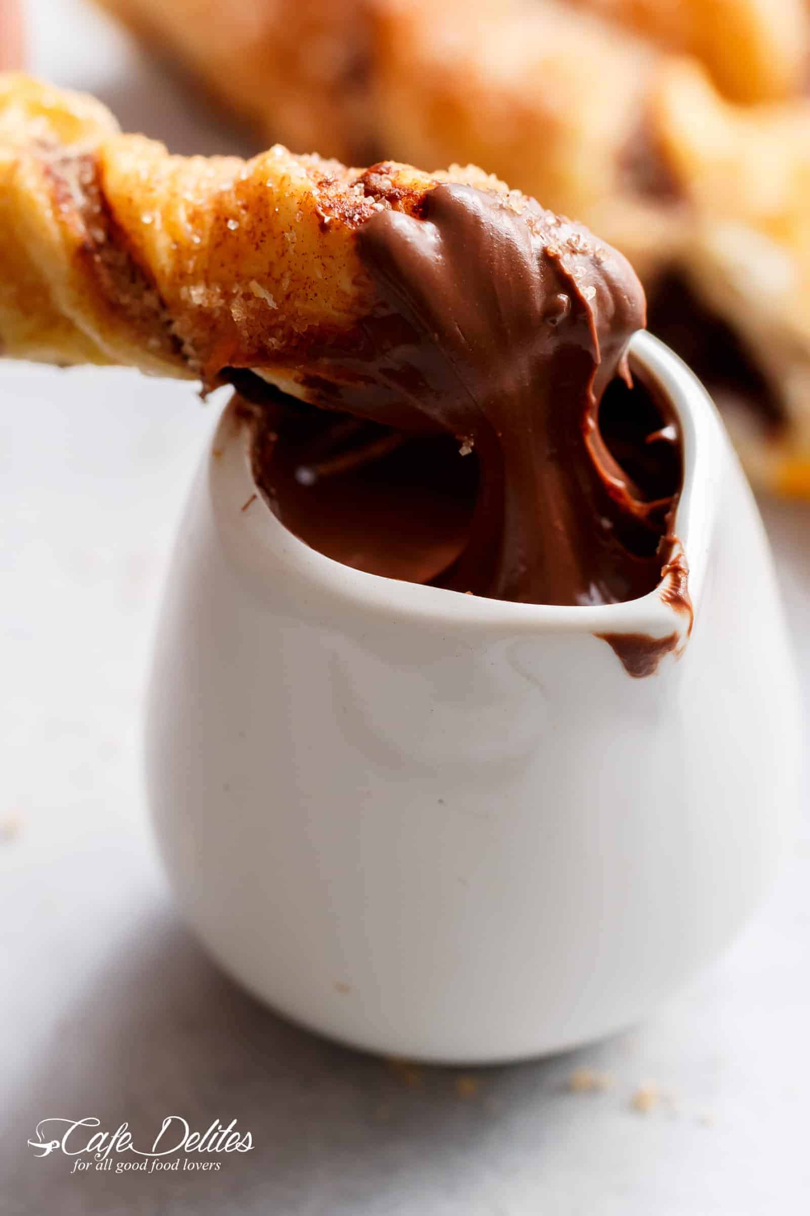close up churro tree branch being sipped in melted chocolate