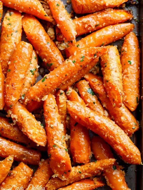 This close-up shot image of showcases a tantalizing dish of roasted carrots. Tightly packed together on a baking sheet, the carrots are a vibrant orange, glistening with a delicious glaze. A scattering of herbs, likely parsley, adds a touch of green and hints at a savory flavor profile. The edges of some carrots are slightly caramelized, promising a delightful sweetness and crunch.