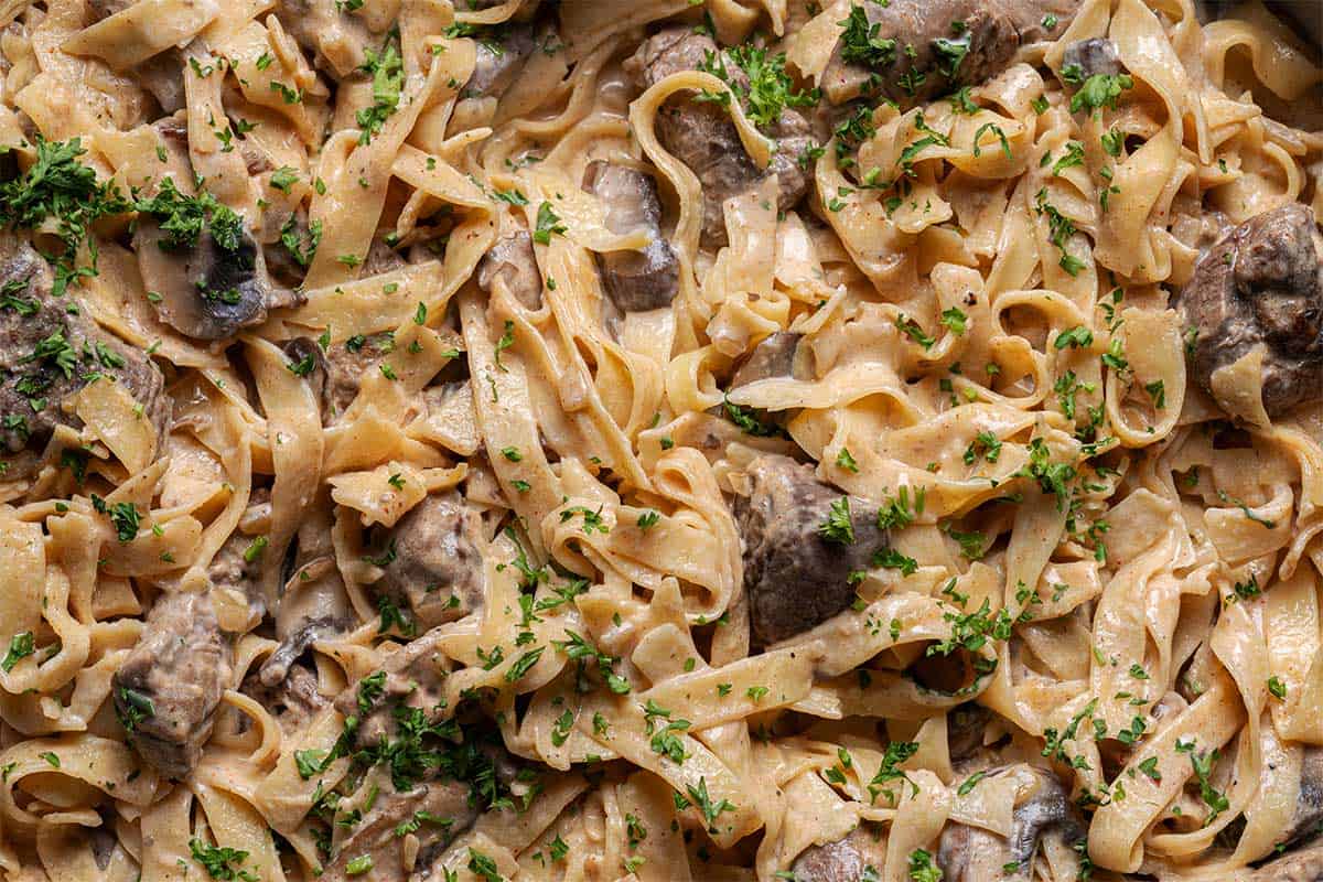 "Top-down view of a creamy pasta dish, featuring tender steak chunks coated in a velvety cream sauce, garnished with fresh parsley leaves for a vibrant touch.