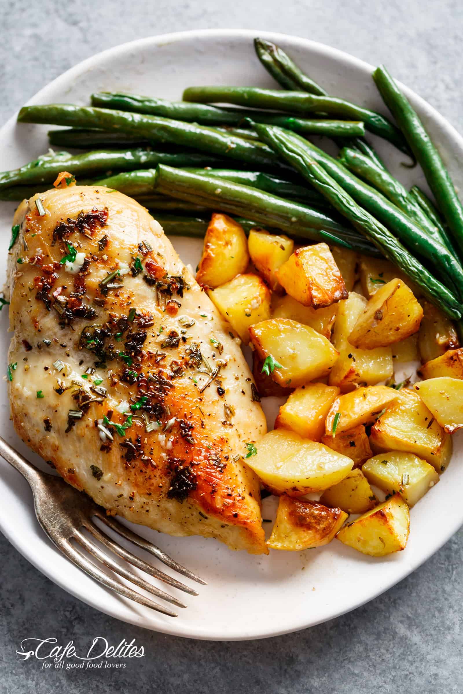 Green beans, crispy potatoes and a golden chicken breast on a white plate with a fork ready to eat.