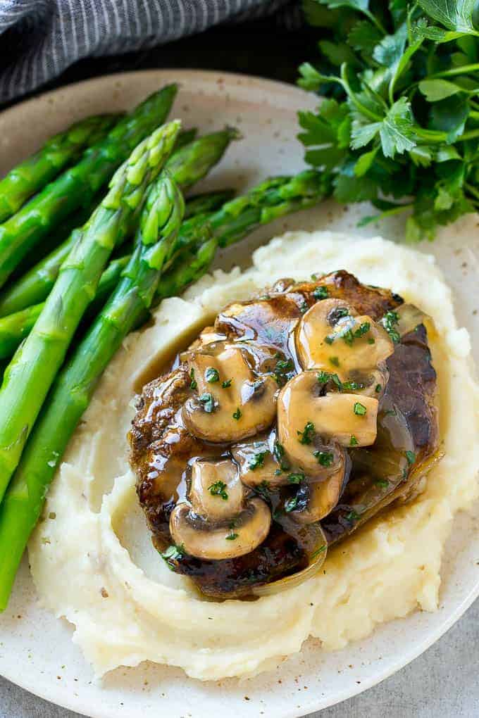 Salisbury steak is perfect served over mashed potatoes with a green vegetable on a fancy plate.