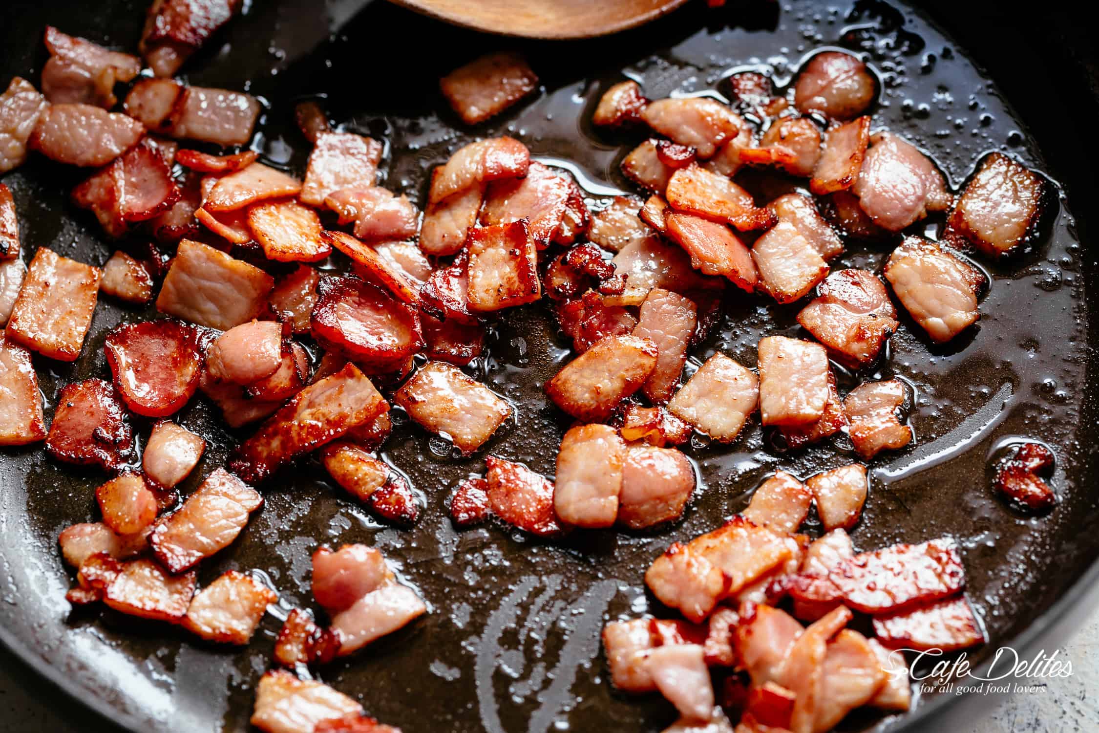 Bacon frying in a black pan with a wooden spoon 