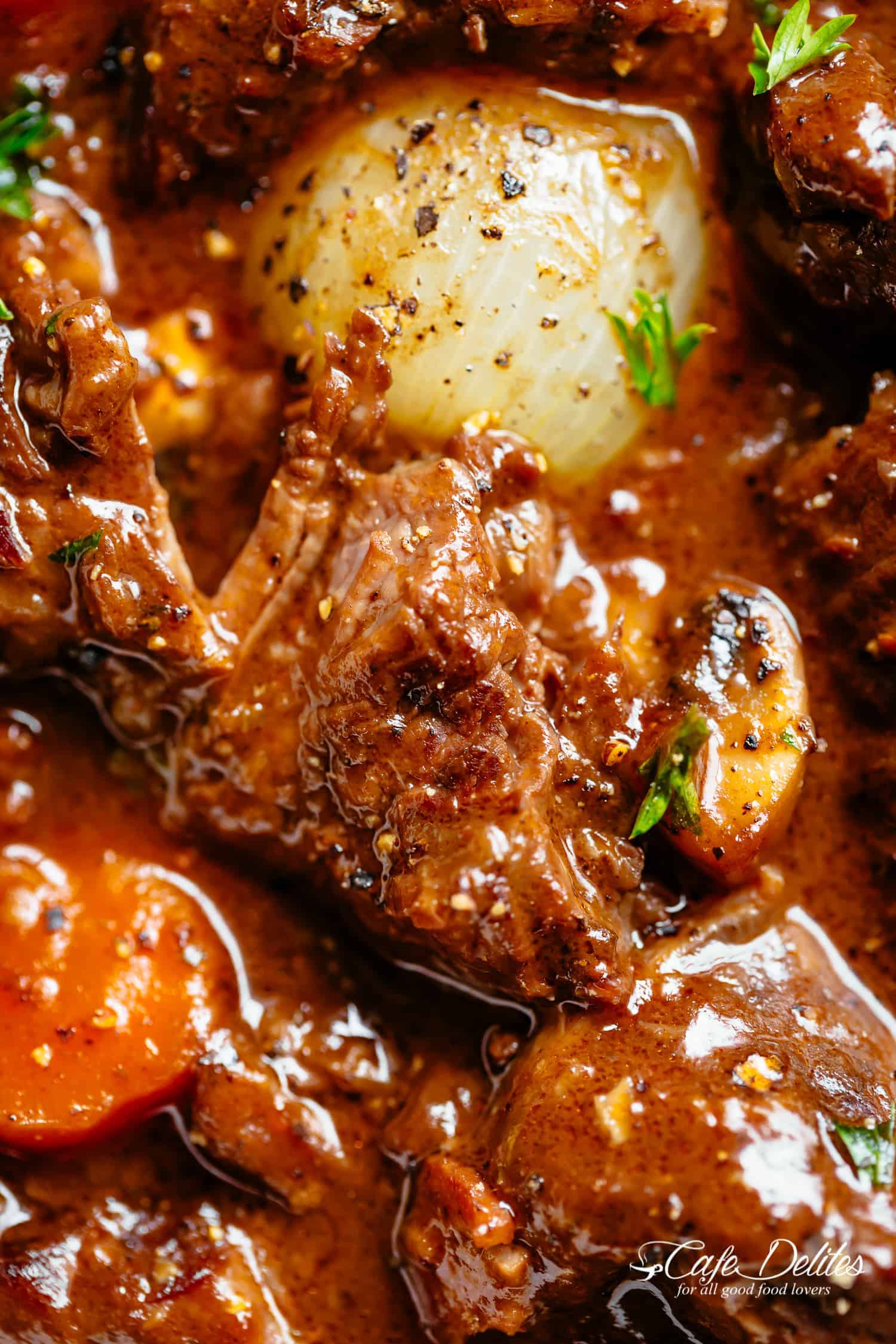 A close up image of a piece of tender fall apart beef pieces simmered in a rich red wine gravy with a white onion and carrots. Garnished with fresh chopped parsley. 