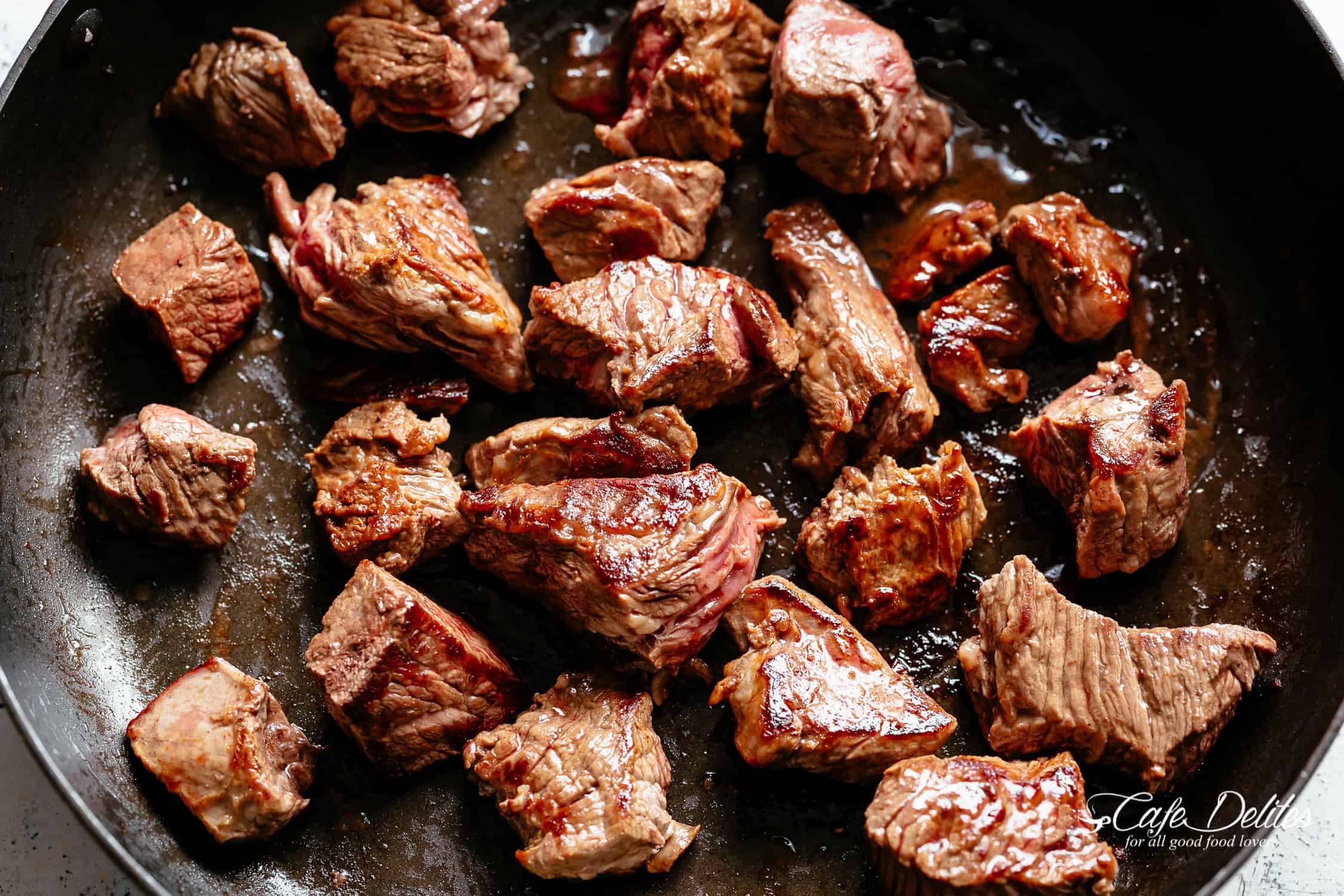 Seared beef pieces in bacon grease in a black pan 