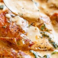 spinach creamy sauce dripping over Tuscan Chicken with sun dried tomatoes, parmesan cheese and