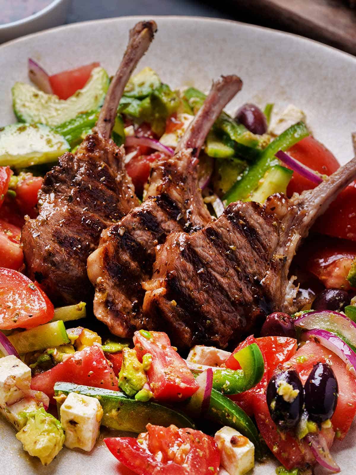 greek lamb chops perfectly seared and juicy sits in the middle of a salad mix in a bowl