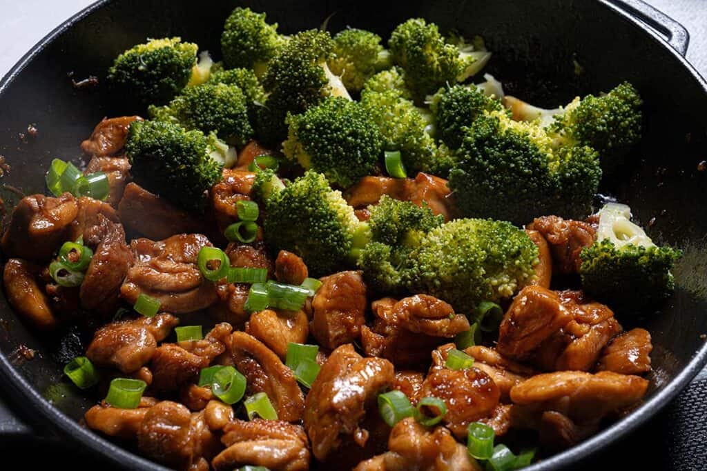 Adding broccoli to the chicken teriyaki in a pan