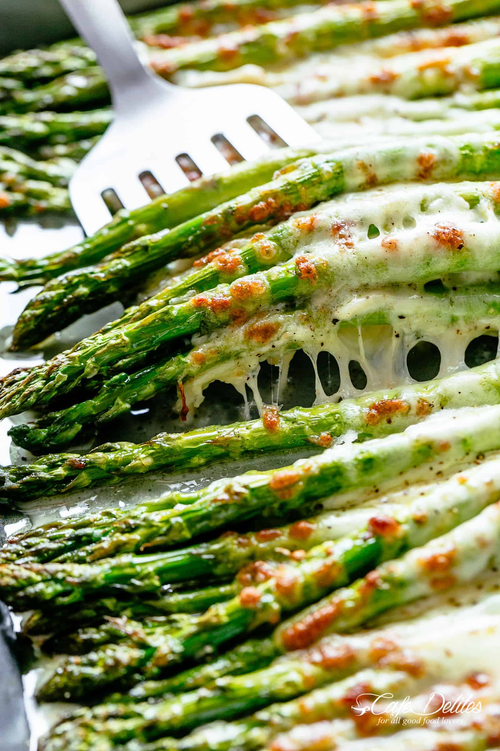 Cheesy Garlic Roasted Asparagus | cafedelites.com A silver spatula picks up a pile of spears asparagus topped with melted mozzarella cheese.