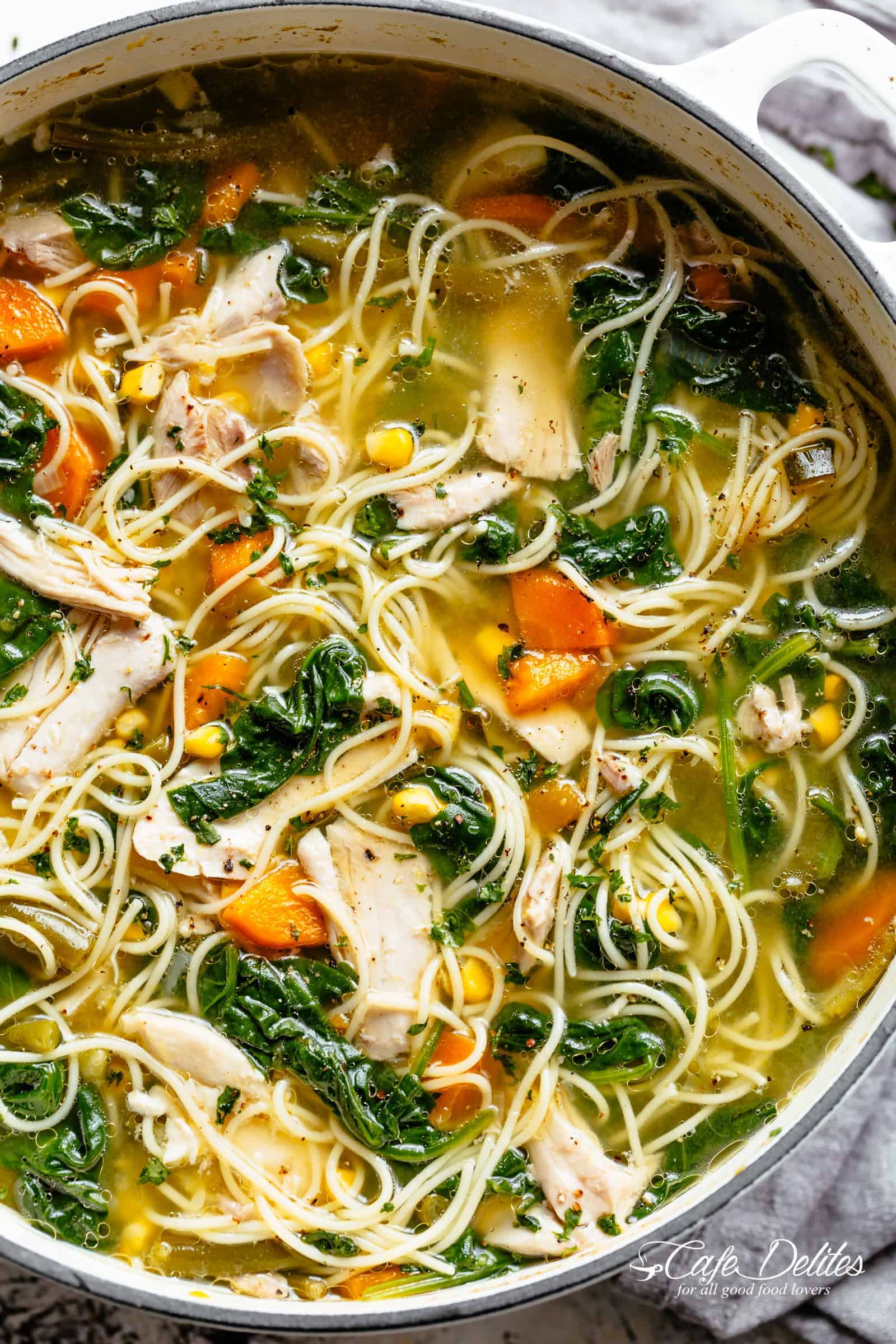 Homemade Chicken Noodle Soup loaded with carrots, spinach, corn and egg noodles mixed through a cloudy broth in a bowl.