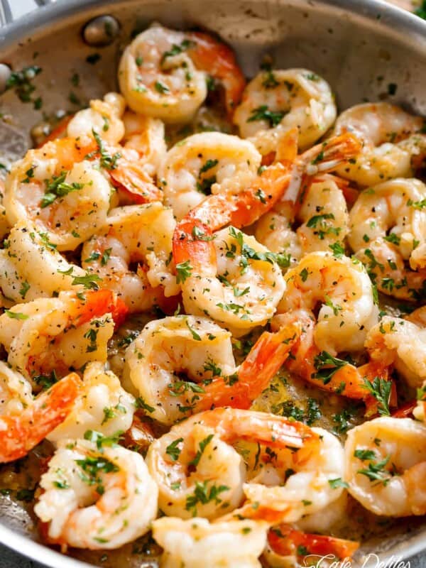 Flavorful shrimp are served in a pan, their pinkish-orange hues suggesting they are cooked to perfection. The shrimp are generously coated in a light sauce, which appears to be infused with herbs, as evidenced by the specks of green throughout the dish.