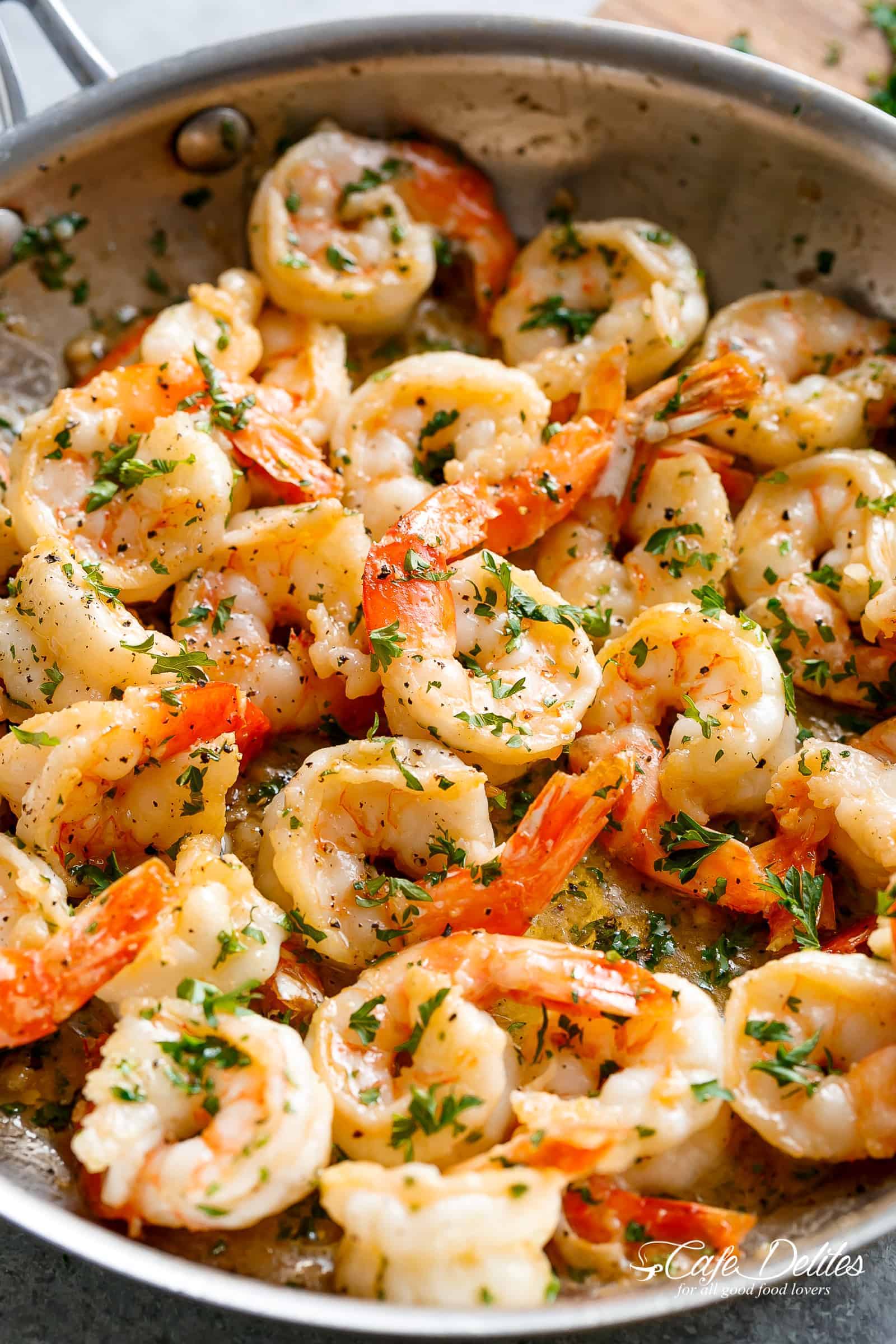Flavorful shrimp are served in a pan, their pinkish-orange hues suggesting they are cooked to perfection. The shrimp are generously coated in a light sauce, which appears to be infused with herbs, as evidenced by the specks of green throughout the dish.