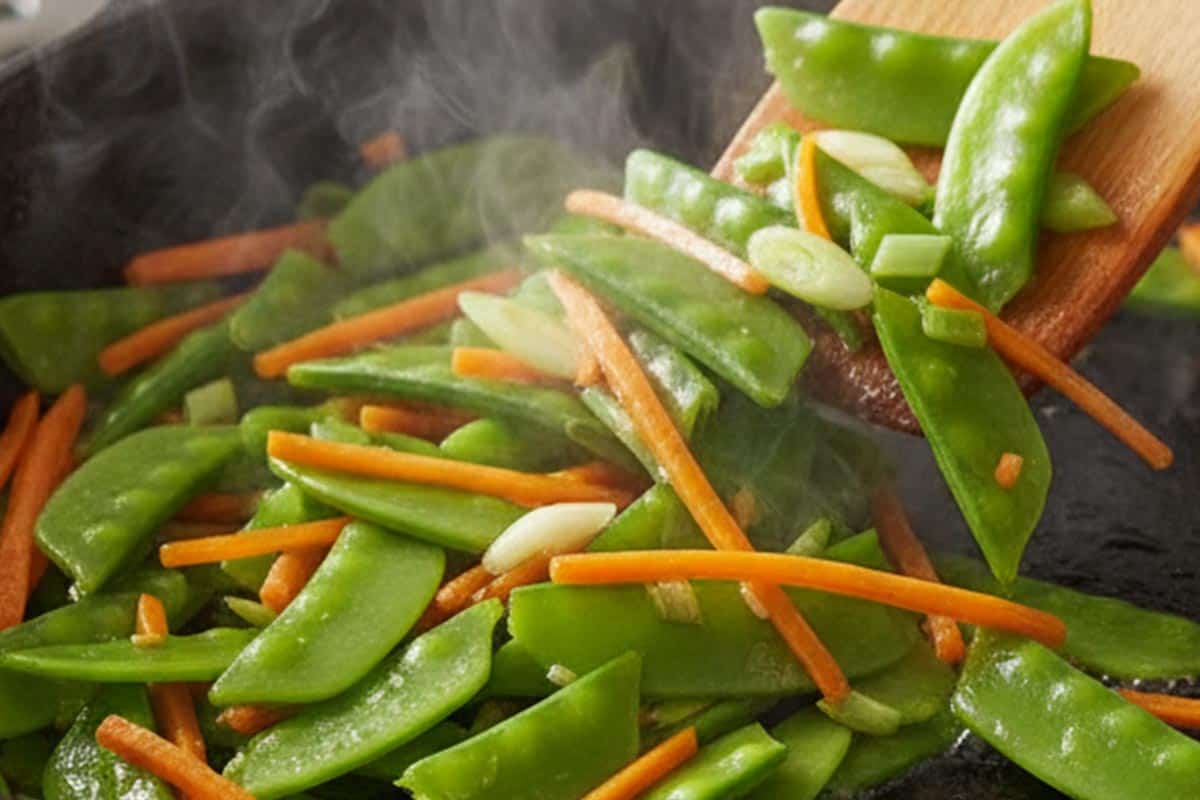 Stir frying the snow peas, carrots, and green onions.
