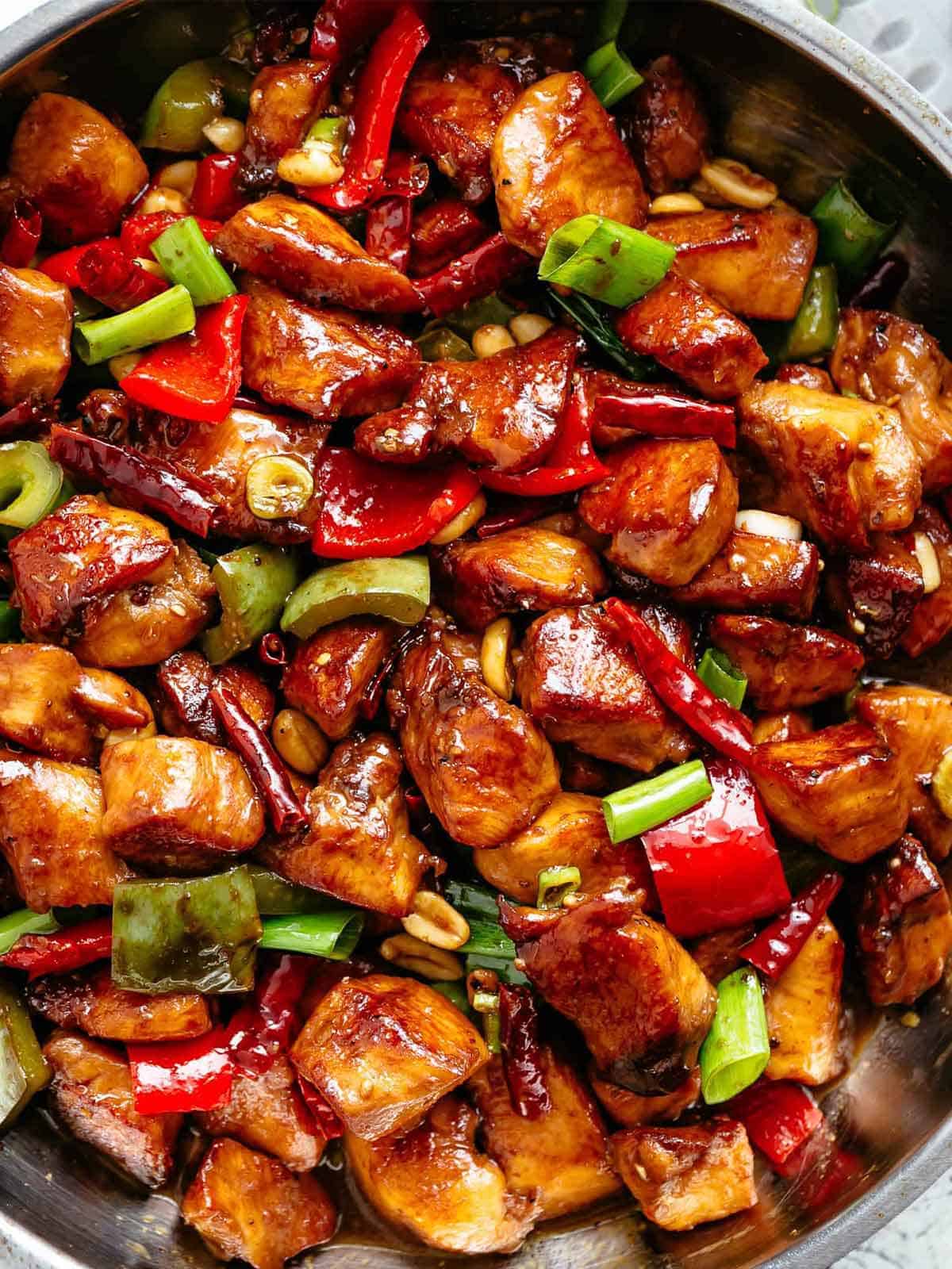 Close up image of Kung Pao Chicken in a sticky Kung Pao sauce with green and red chopped vegetables picked in with chicken pieces. 