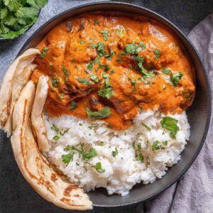 chicken tikka masala in a bowl garnished with fresh parsley, served beside rice