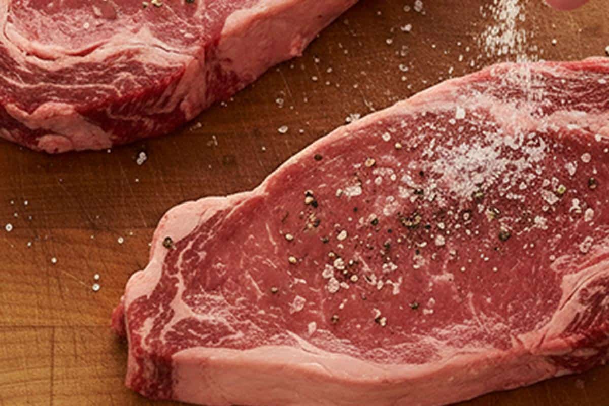 Seasoning the steaks with salt and pepper.