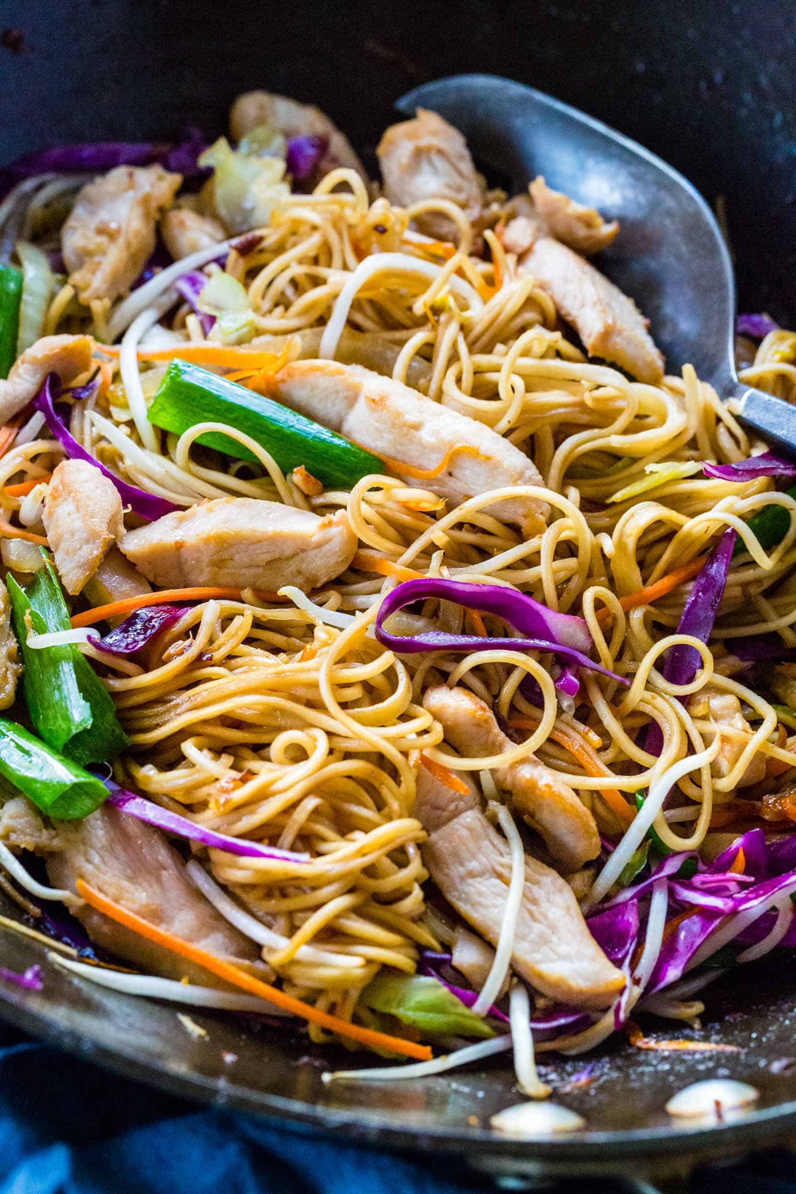 Wok spatula mixing chicken chow mein in a pan