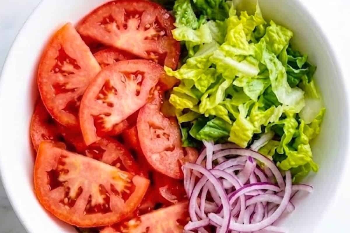 In a large serving bowl, combine the sliced tomatoes, shredded romaine lettuce, and thinly sliced red onion and mix the ingredients.