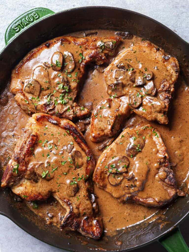 Top view of creamy pork chops in a skillet, topped with chunky mushroom pieces and a sprinkle of fresh parsley.