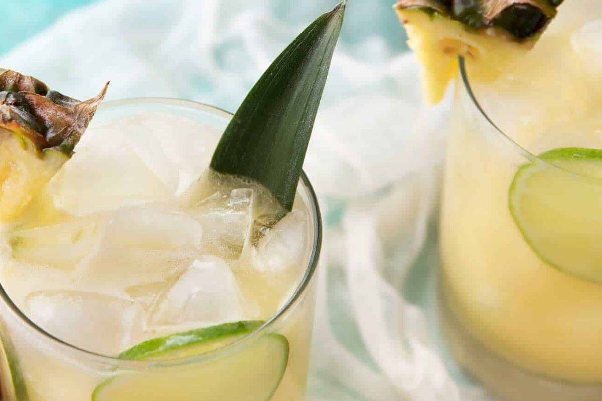 Fill two glasses with ice and divide the mixture between them. Top with ginger ale, stir gently, and finish with pineapple wedges, lime slices, and a pineapple leaf.