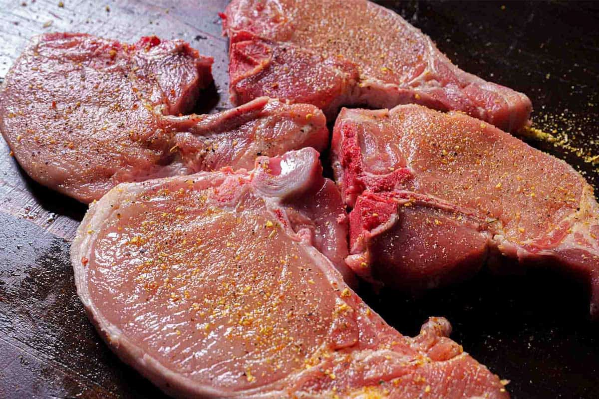Chops being generously seasoned with seasoning salt and pepper, ready to soak up bold flavors.