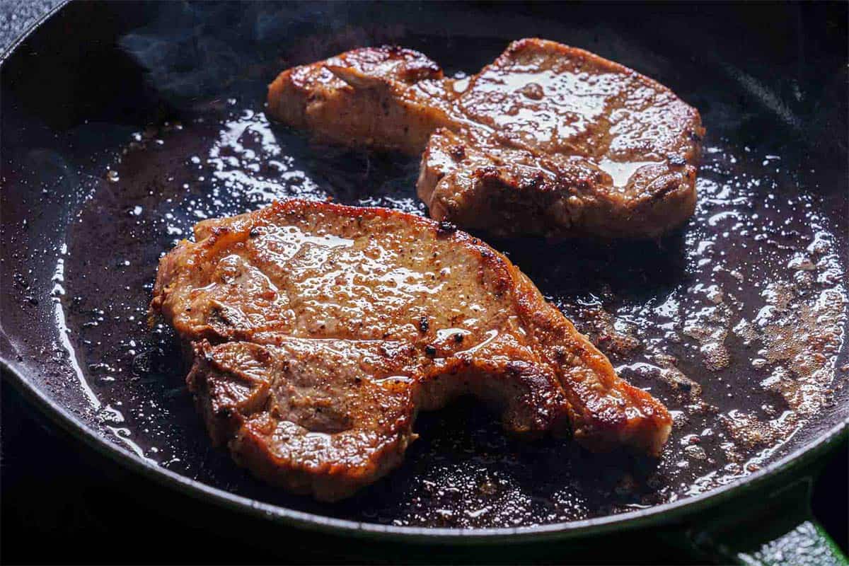 Chops sizzling in the pan, seared over medium-high heat to achieve a golden brown crust.