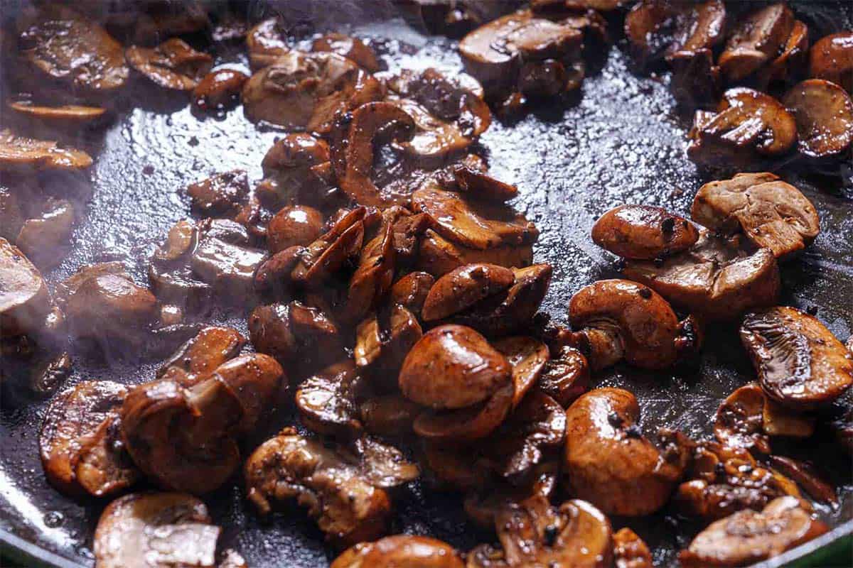 Mushrooms being added to the pan, soaking up the rich, buttery juices from the meat for enhanced flavor.