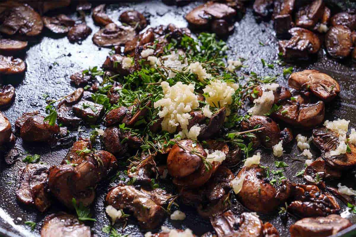 Garlic and parsley being sprinkled into the mushrooms, ready to be sautéed until fragrant and flavorful.