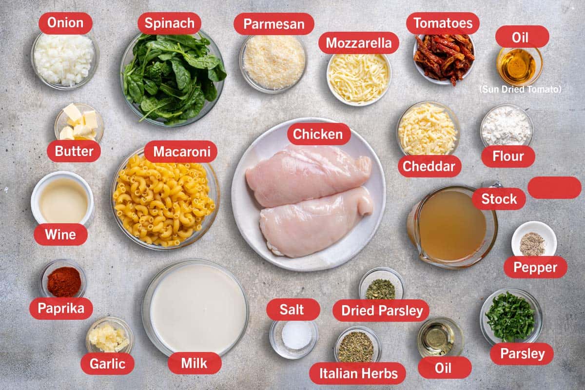 Image of all the ingredients needed for the preparation of this recipe, specifically: onion, spinach, parmesan, mozzarella, tomatoes, oil from sun dried tomatoes, butter, wine, macaroni, chicken, cheddar, flour, stock, paprika, garlic, milk, salt, dried parsley, italian herbs, oil, parsley