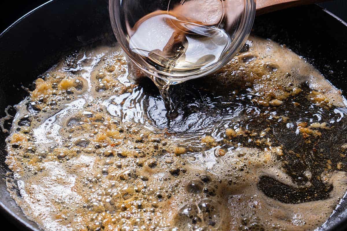 An image of white wine being added to the skillet where garlic is being sautéed together with butter.