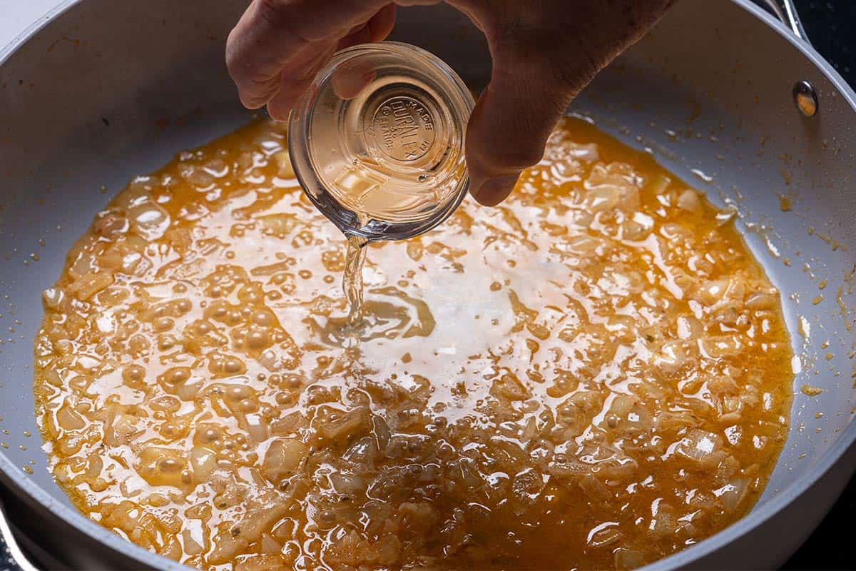 Wine being poured into the pan, enhancing the flavors of the sautéed aromatics as they cook.