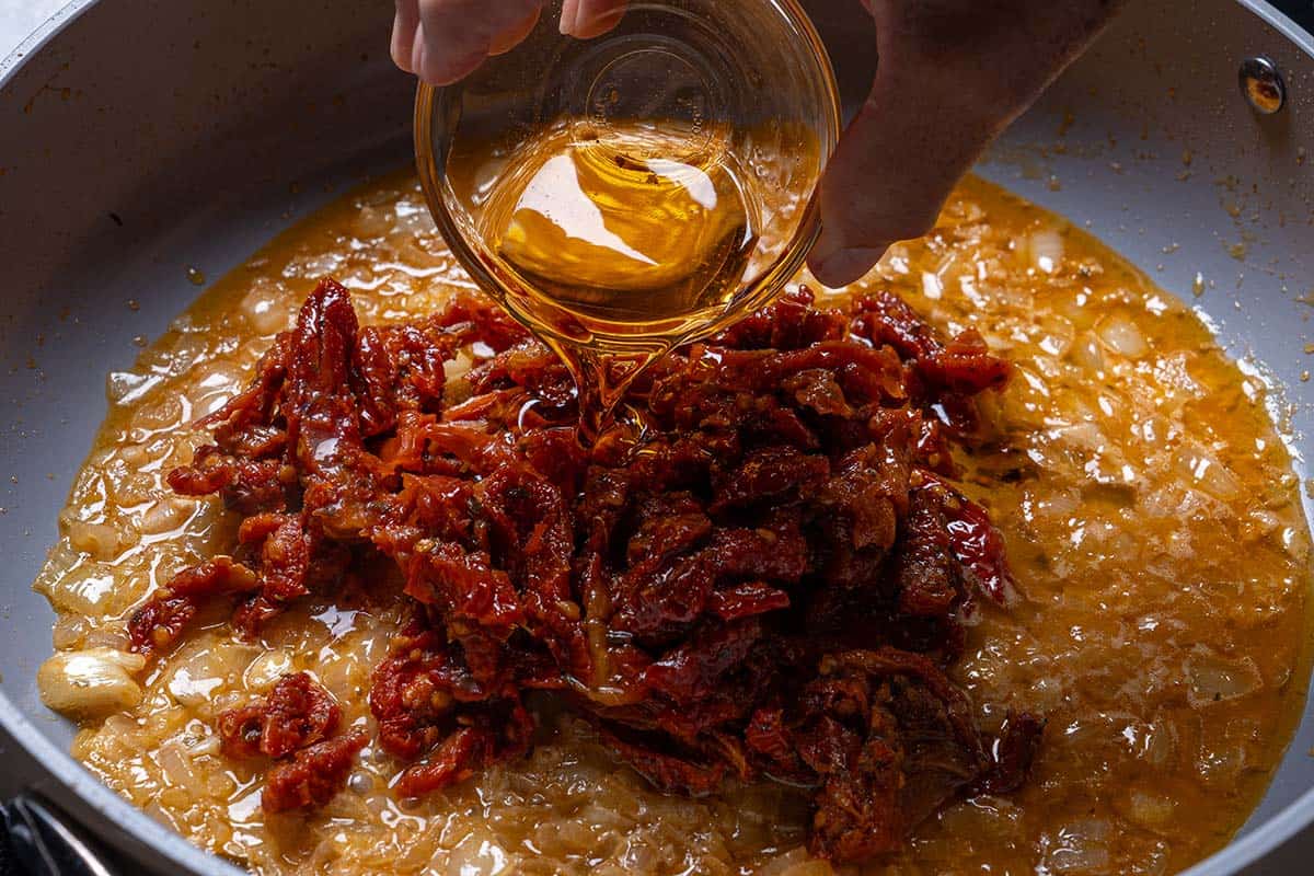 Sun-dried tomatoes and their infused oil being added to the pan, releasing rich, tangy flavors into the dish.