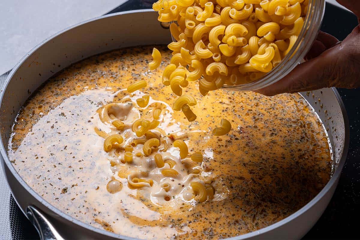 Dry macaroni being poured into the creamy sauce, ready to cook until perfectly 'al dente.