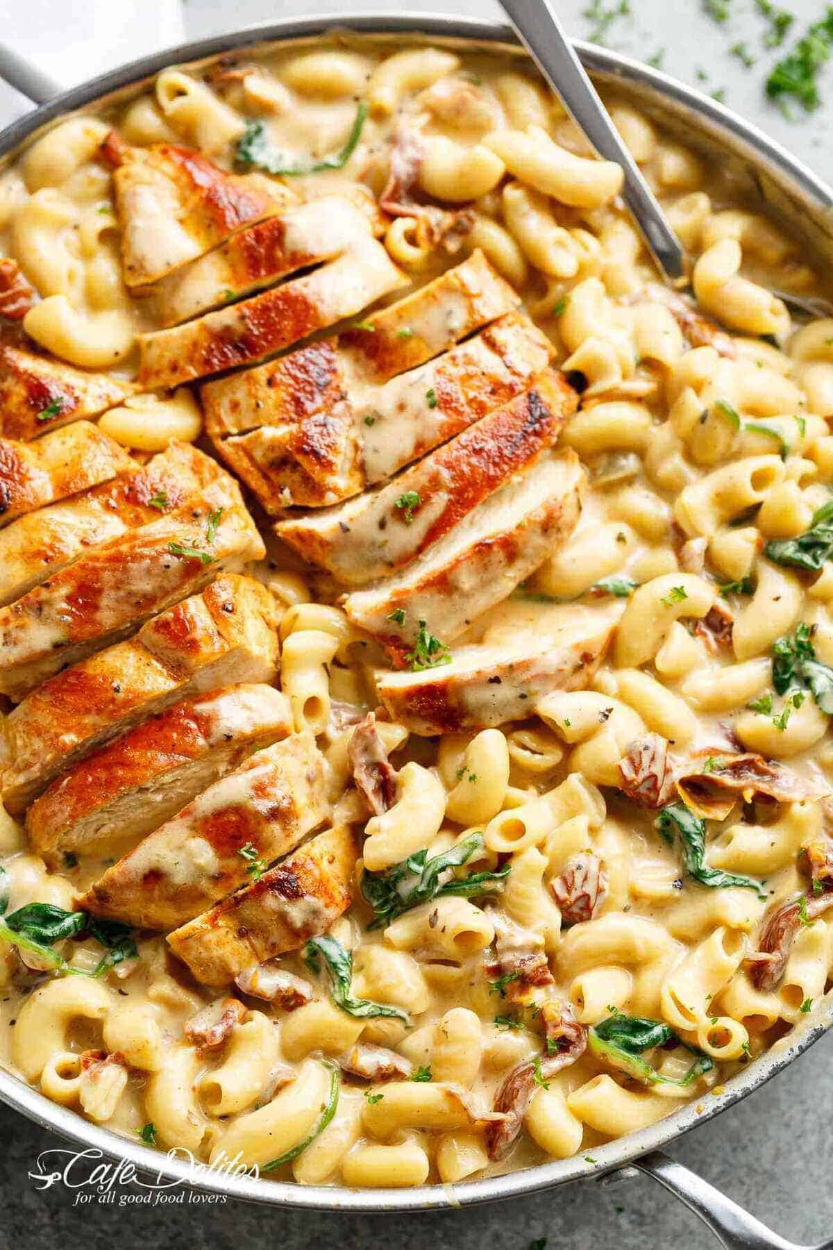 Tuscan chicken sliced, on top of a bed of creamy pasta with sundered tomatoes and spinach with Fresh herbs sprinkled on top.