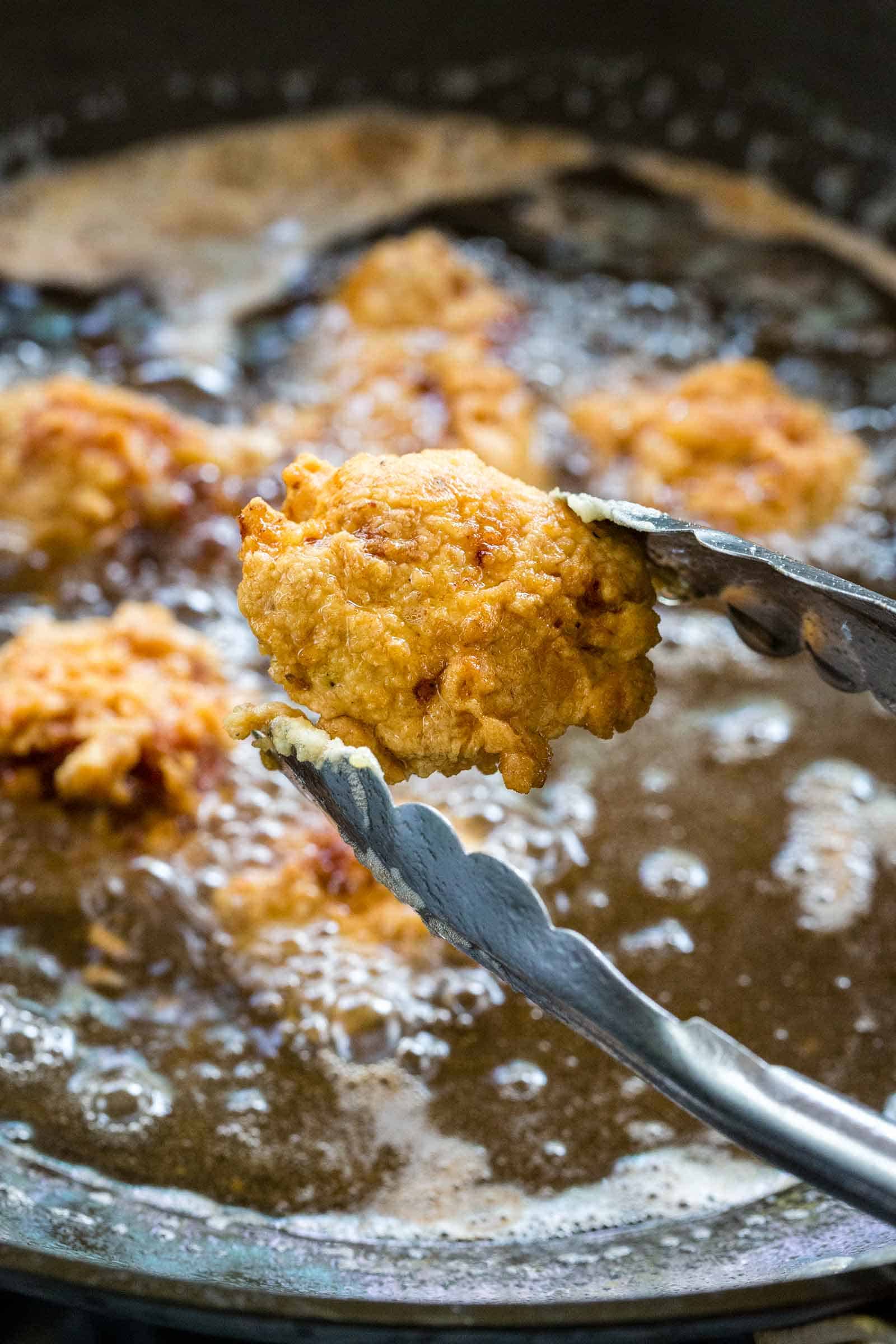 metal tongs holding up a piece of deep fried pork from oil