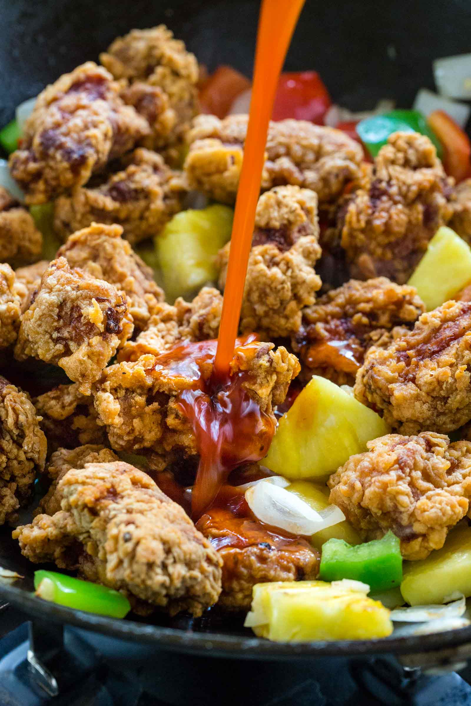 sauce pouring into a wok filled with pork and vegetables