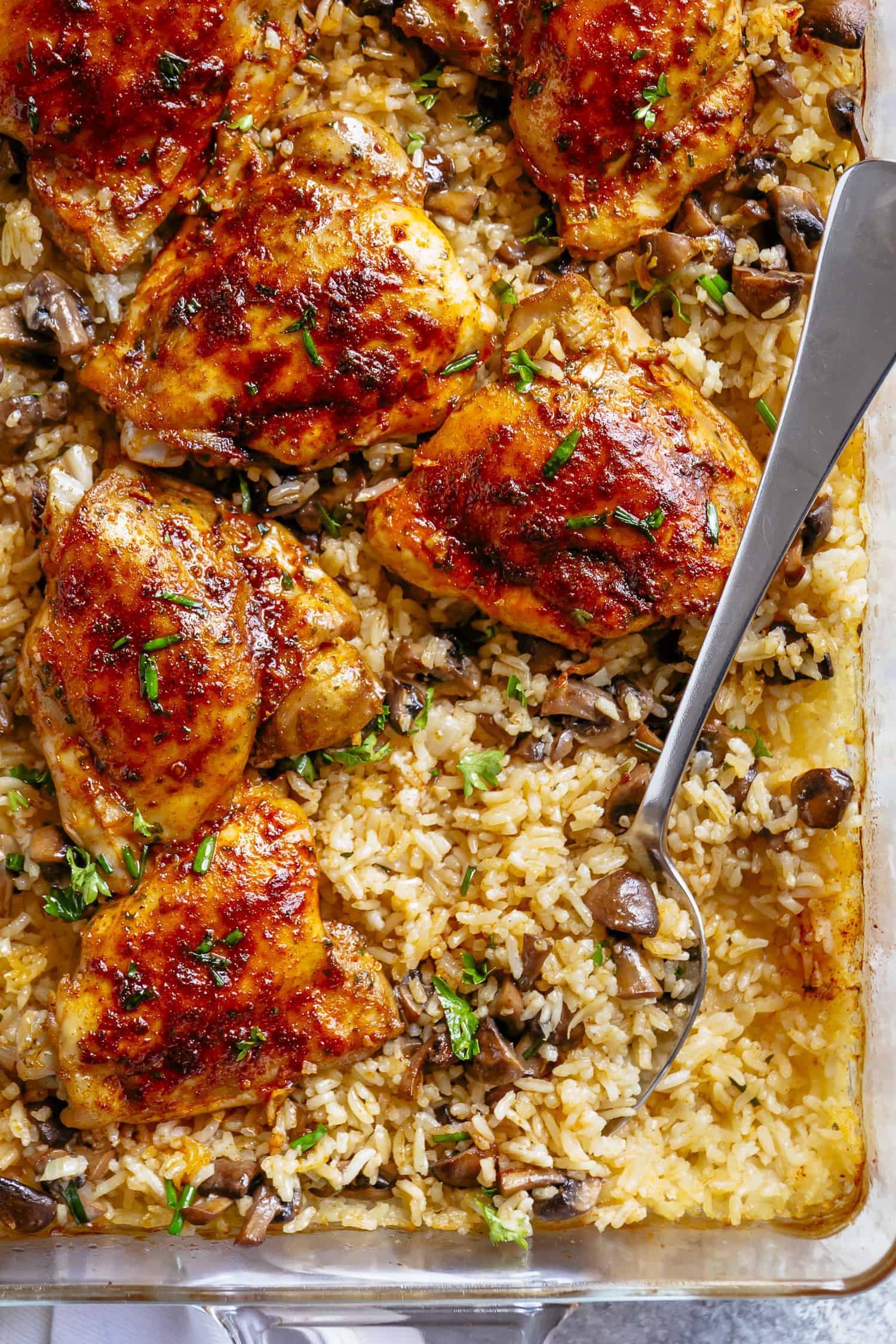Top view of Gold chicken thighs on top of a bed of yellow rice and mushrooms, topped with chopped, fresh, green herbs. 