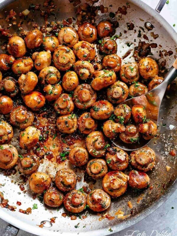 Image of button mushrooms coated in garlic butter sauce, simmering in a pan, ready to be scooped with a kitchen spoon.