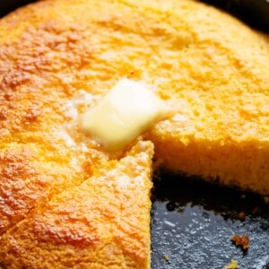 Cornbread with a triangle slice missing and melting butter cube in top in the centre in a cast iron pan