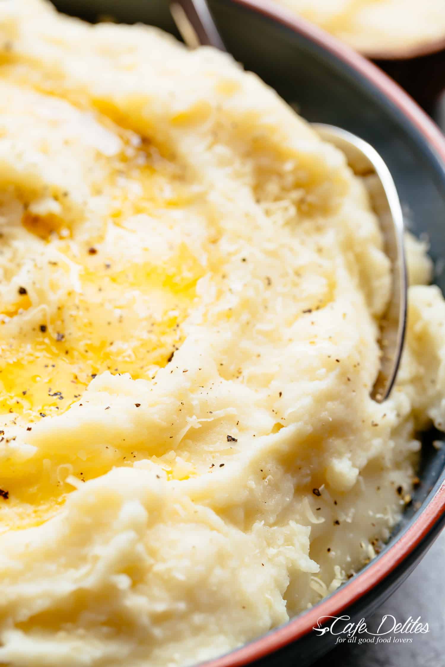 CREAMY Mashed Cauliflower Close-up image of buttery cauliflower topped with parmesan, oil, and cracked pepper.