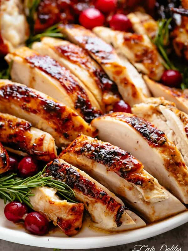 Slices of Roast Turkey on a white plate garnished with cranberries and rosemary sprigs.