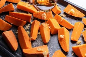 Sweet potatoes on a baking tray being drizzled with oil and topped with garlic.