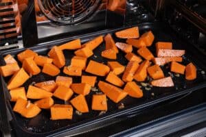 Sweet potatoes roasting in the oven on a baking tray.