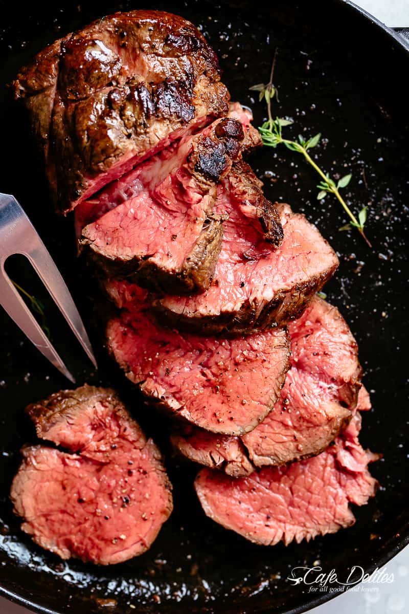 Juicy roasted Beef Tenderloin sliced to show the juicy pink meat, in a black skillet.