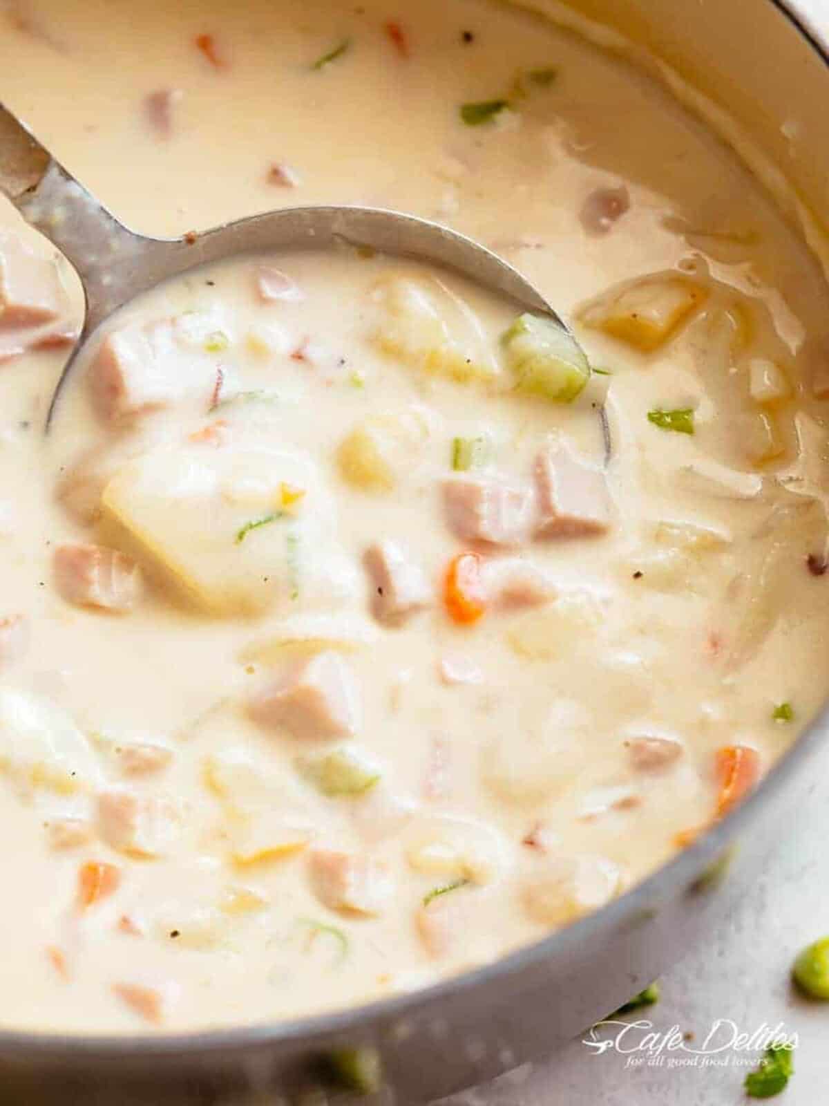 The best Ham and Potato Soup in a pot with a ladle #cafedelites #ham #pot #lecreuset #potatoes Image of creamy ham and potato soup being scooped up by a spoon, ready to be enjoyed.