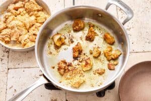 chicken dice being fried in a large skillet with oil.