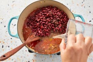 Adding broth to the pot with beef and beans